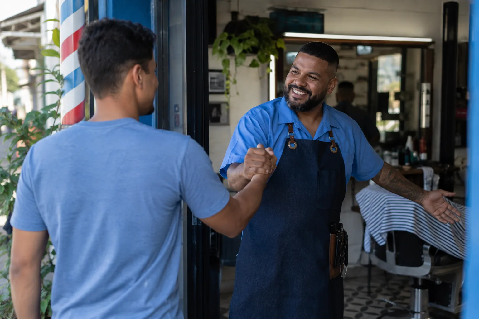 Barbeiro recebe um cliente na porta da barbearia com um aperto de mão