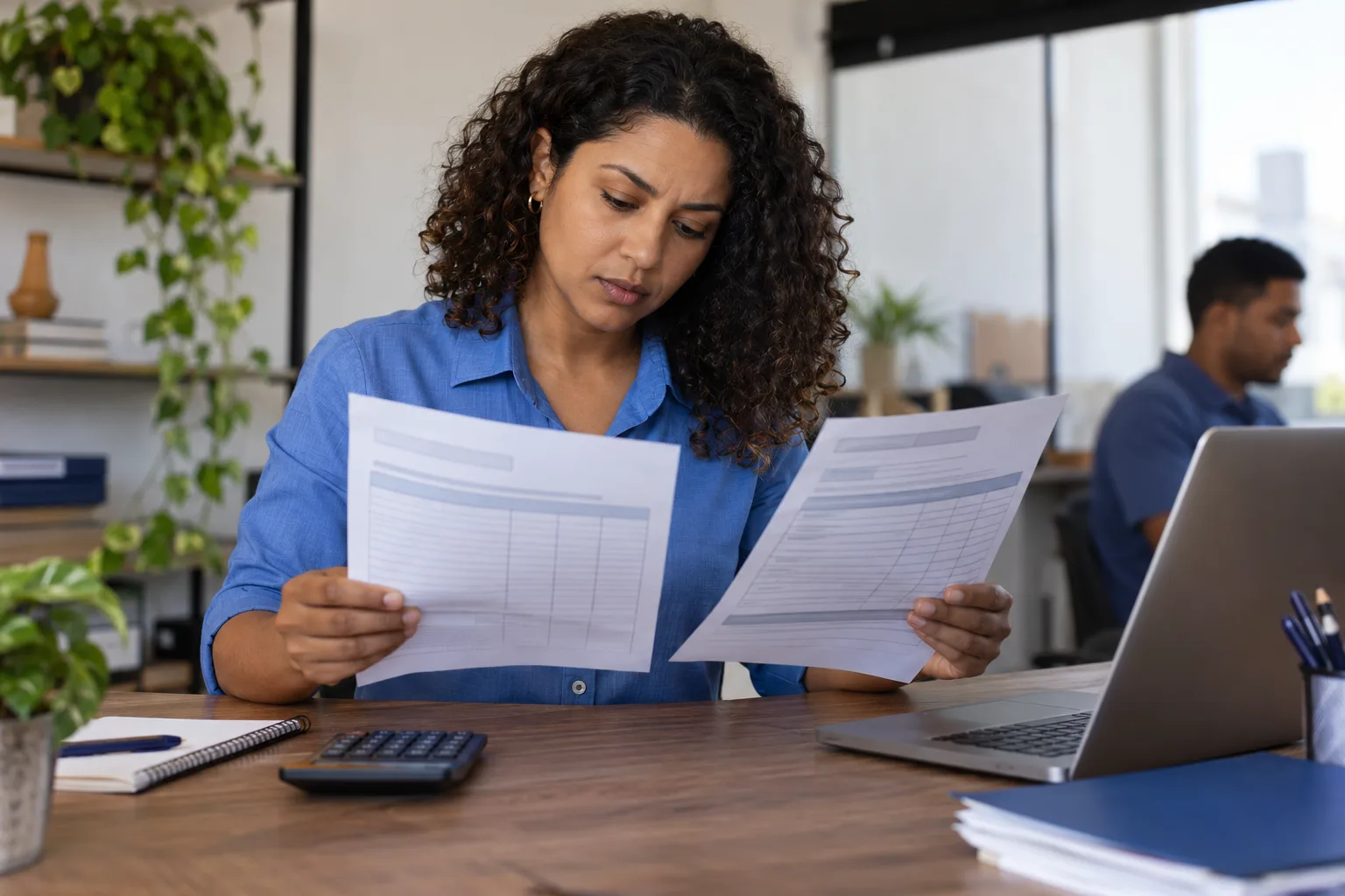 Contadora compara duas notas fiscais impressas com calculadora e notebook na mesa