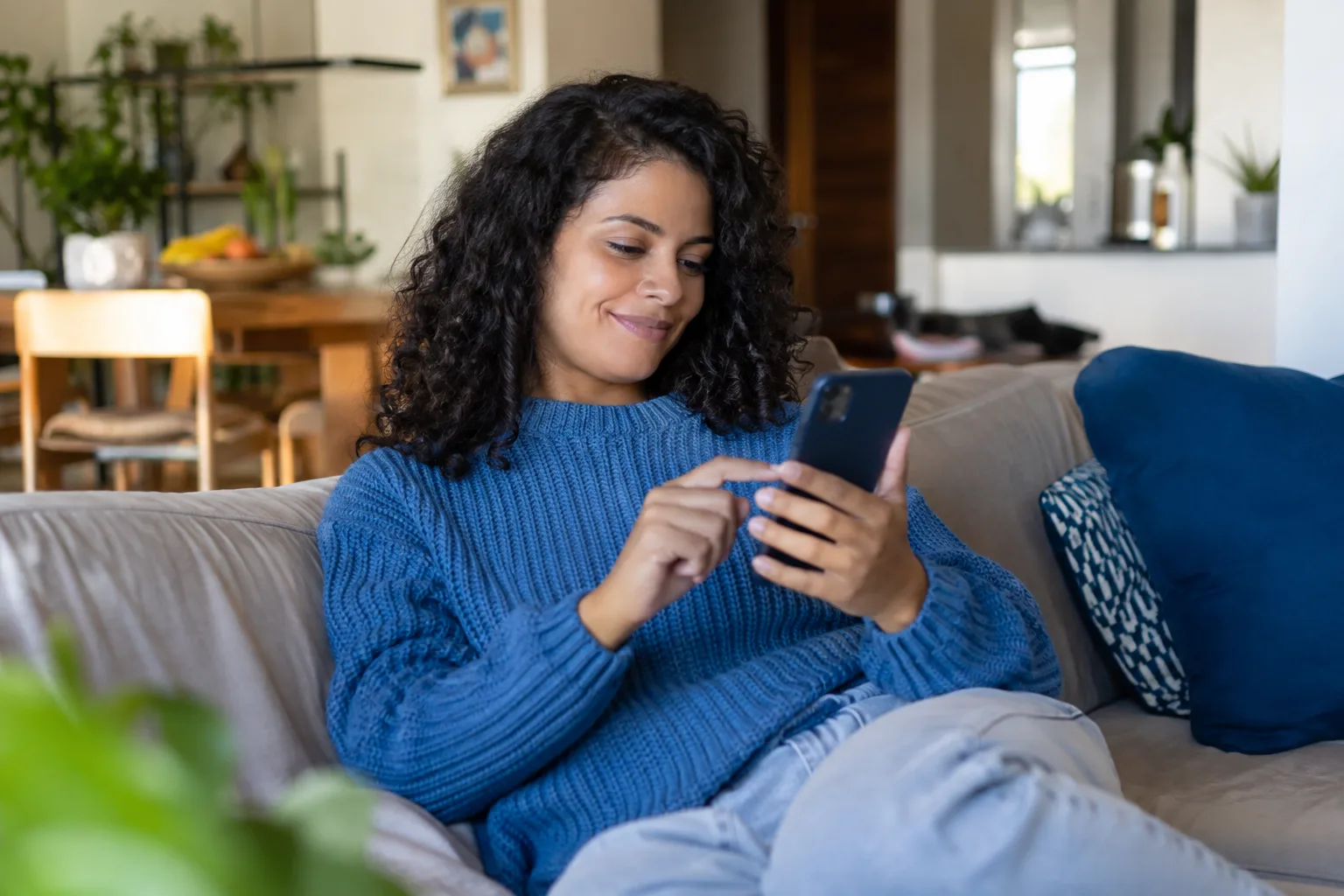 Mulher aprova um pagamento no celular sentada no sofá de casa