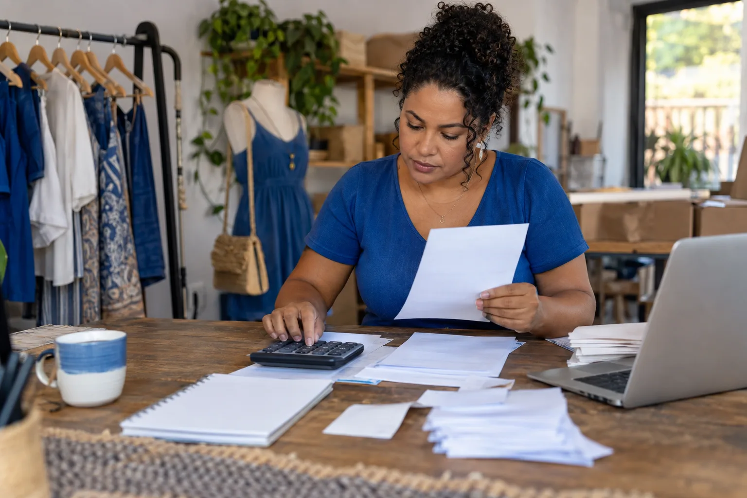 Empreendedora organiza contas e extratos bancários na mesa com calculadora