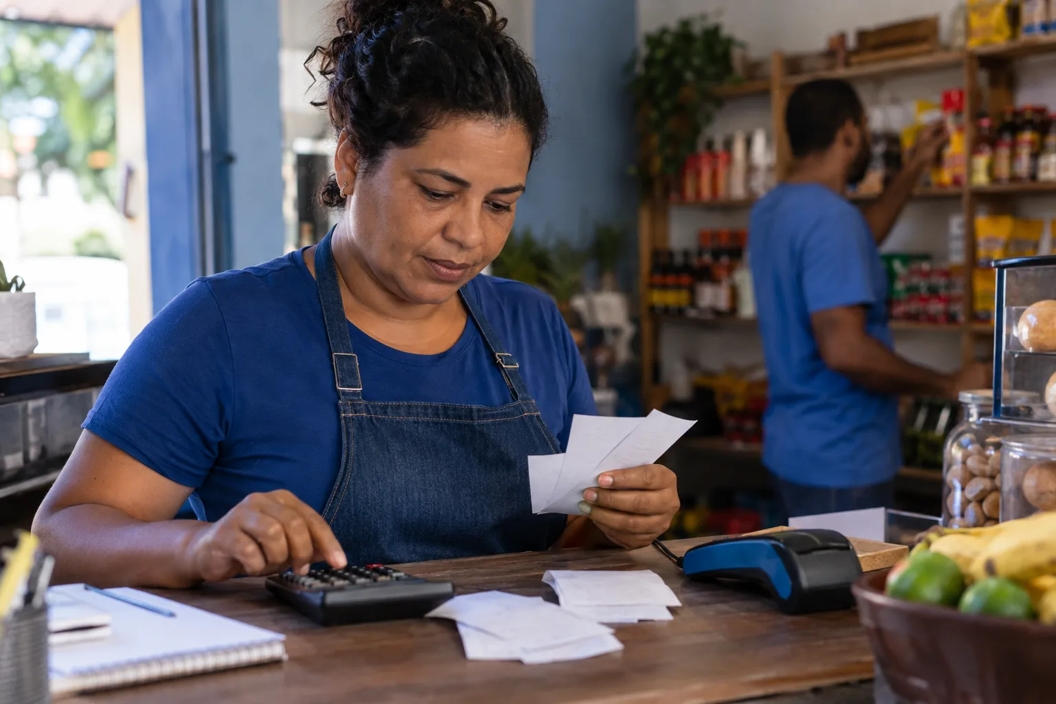 Lojista confere comprovantes da maquininha com calculadora no balcão