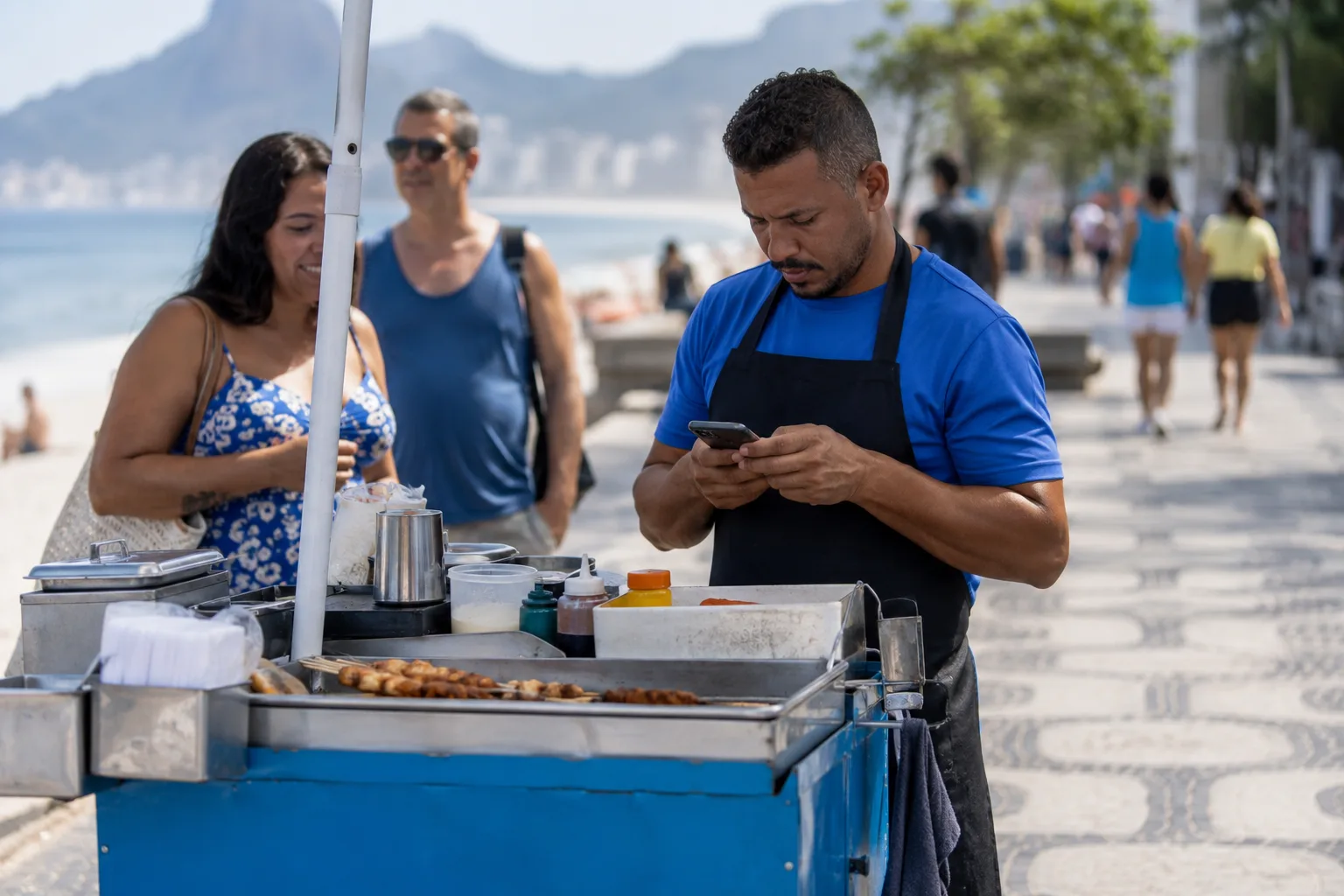 Vendedor de comida de rua confere boletos no celular ao lado do carrinho
