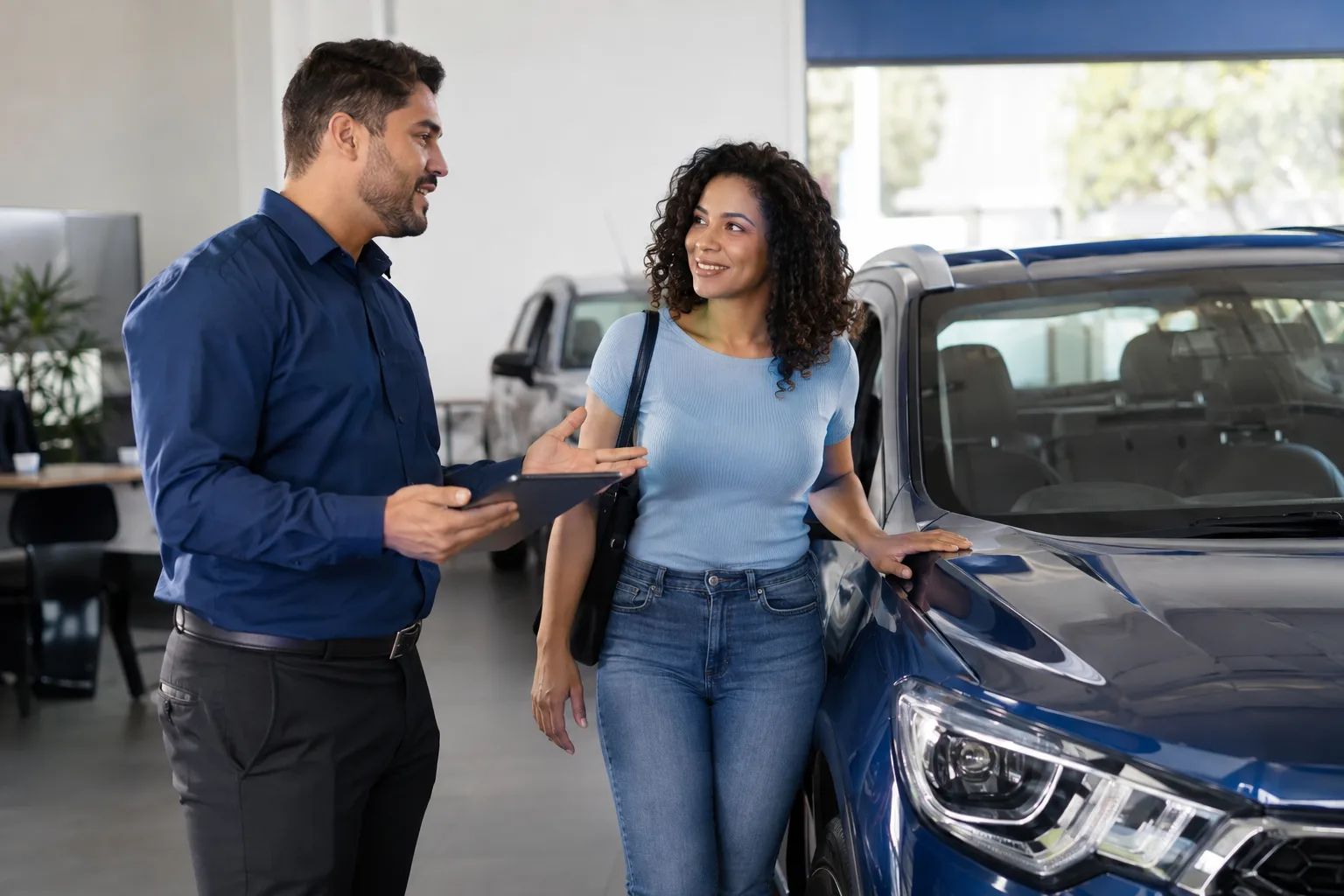 Vendedor de concessionária conversa com cliente ao lado de um carro novo no showroom