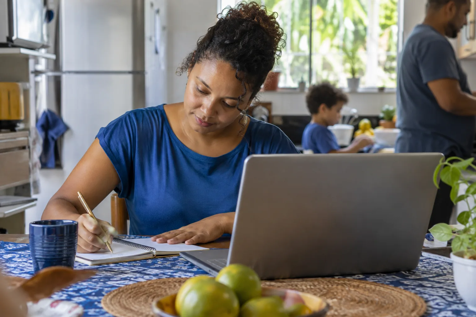 Empreendedora anota as vendas do mês no caderno ao lado do notebook em casa