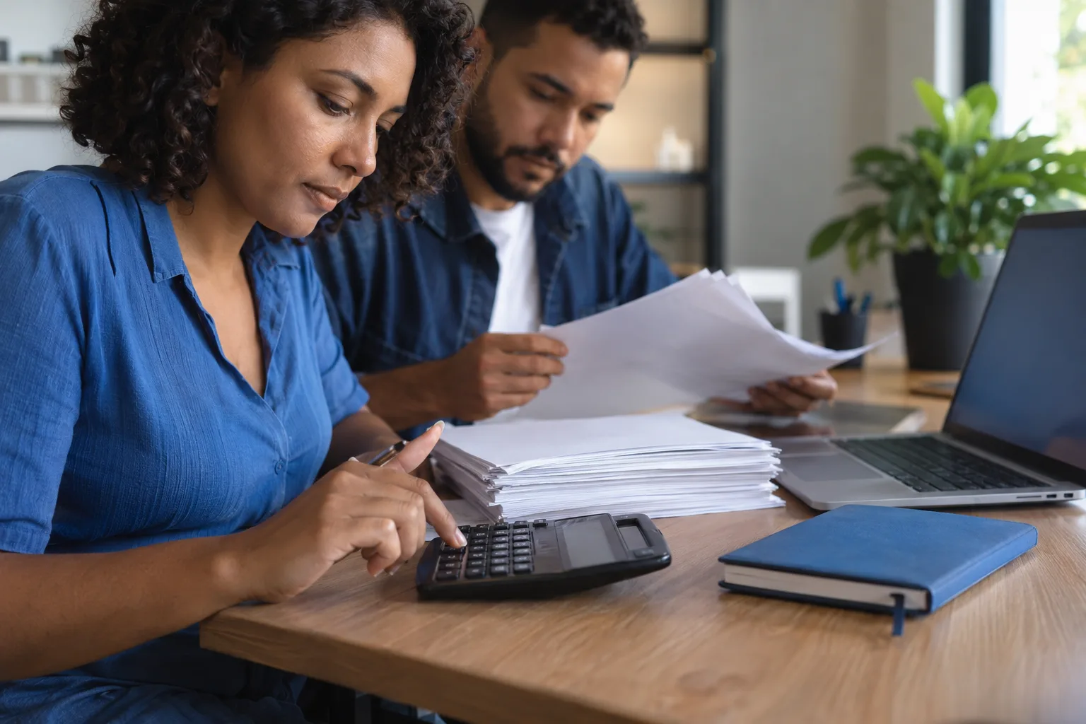 Mãos usam calculadora ao lado de notas fiscais impressas e um notebook no escritório