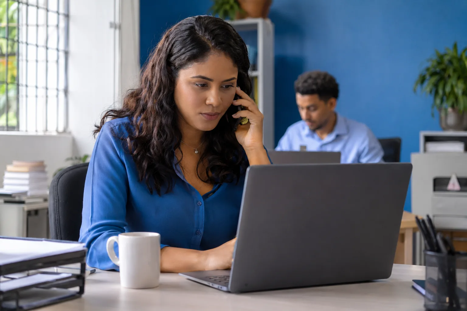Assistente financeira fala ao telefone com um cliente enquanto confere valores no notebook