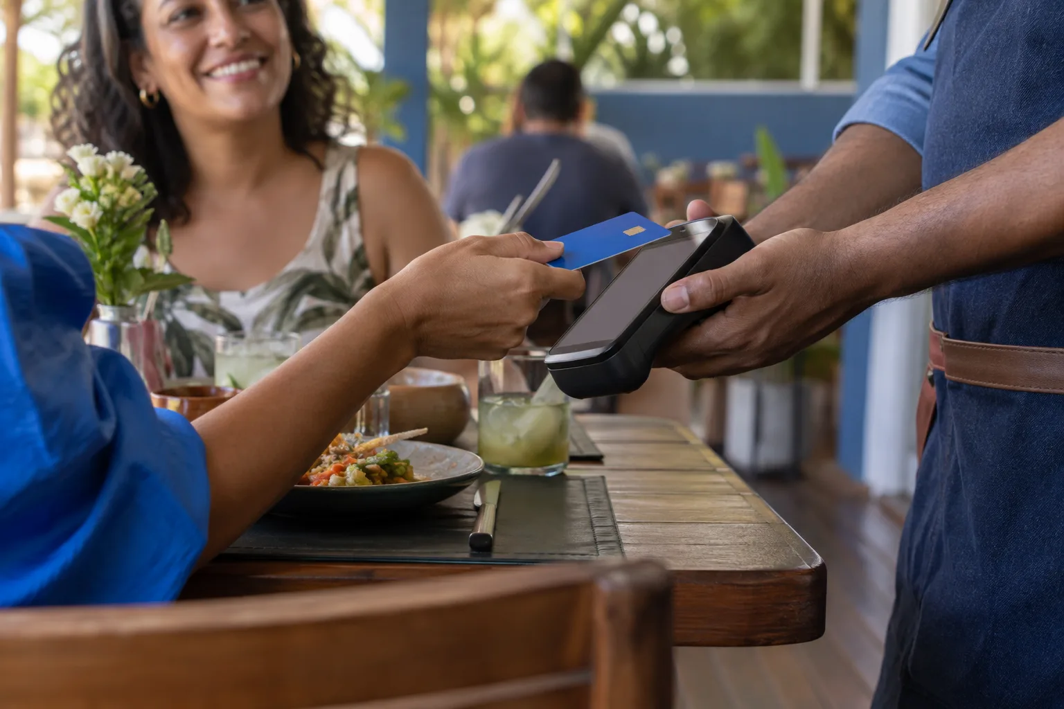 Cliente paga com cartão na maquininha segurada pelo garçom à mesa